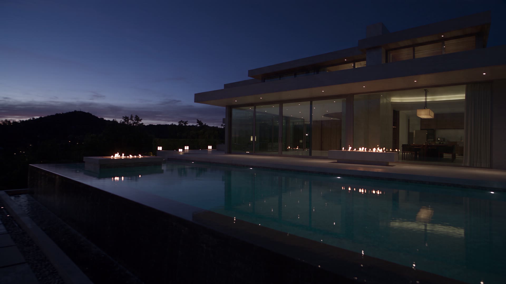 Twilight view of a modern glass estate with an infinity pool, lit for evening